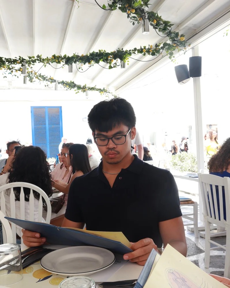 Emmanuel Cabural, founder of Million Design Labs, reading a menu at a sunny outdoor restaurant